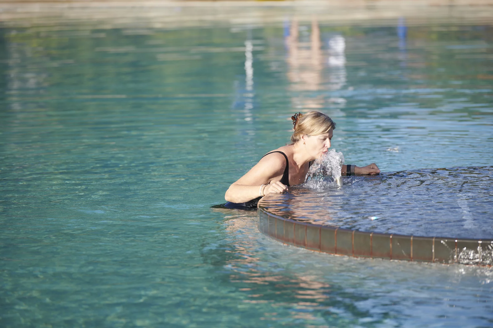 Trinkbrunnen im Aussenbecken im Mineralbad Berg Eine Frau trinkt das naturbelassene und stark kohlensäurehaltige Mineralwasser aus dem Trinkbrunnen im Aussenbecken im Mineralbad Berg.
