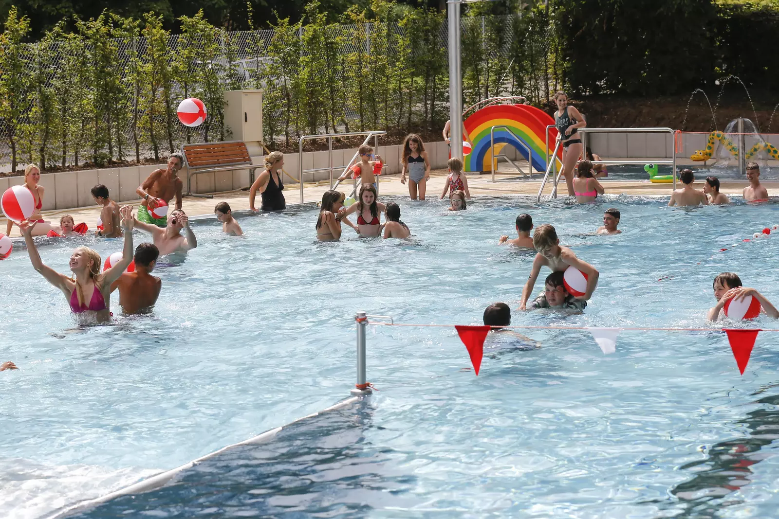 Kinder planschen und spielen Wasserball im Außenschwimmbecken im Freibad Sillenbuch.
