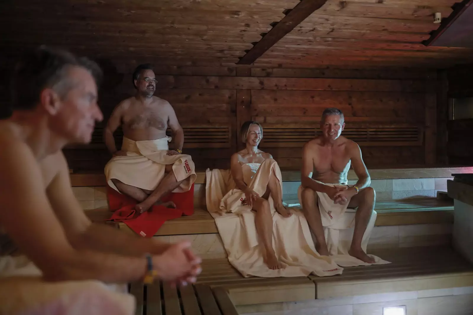 Drei Männer und eine Frau, in Badetücher gehüllt sitzen auf den Holzbänken in der abgedunkelten Kelosauna im LEUZE.