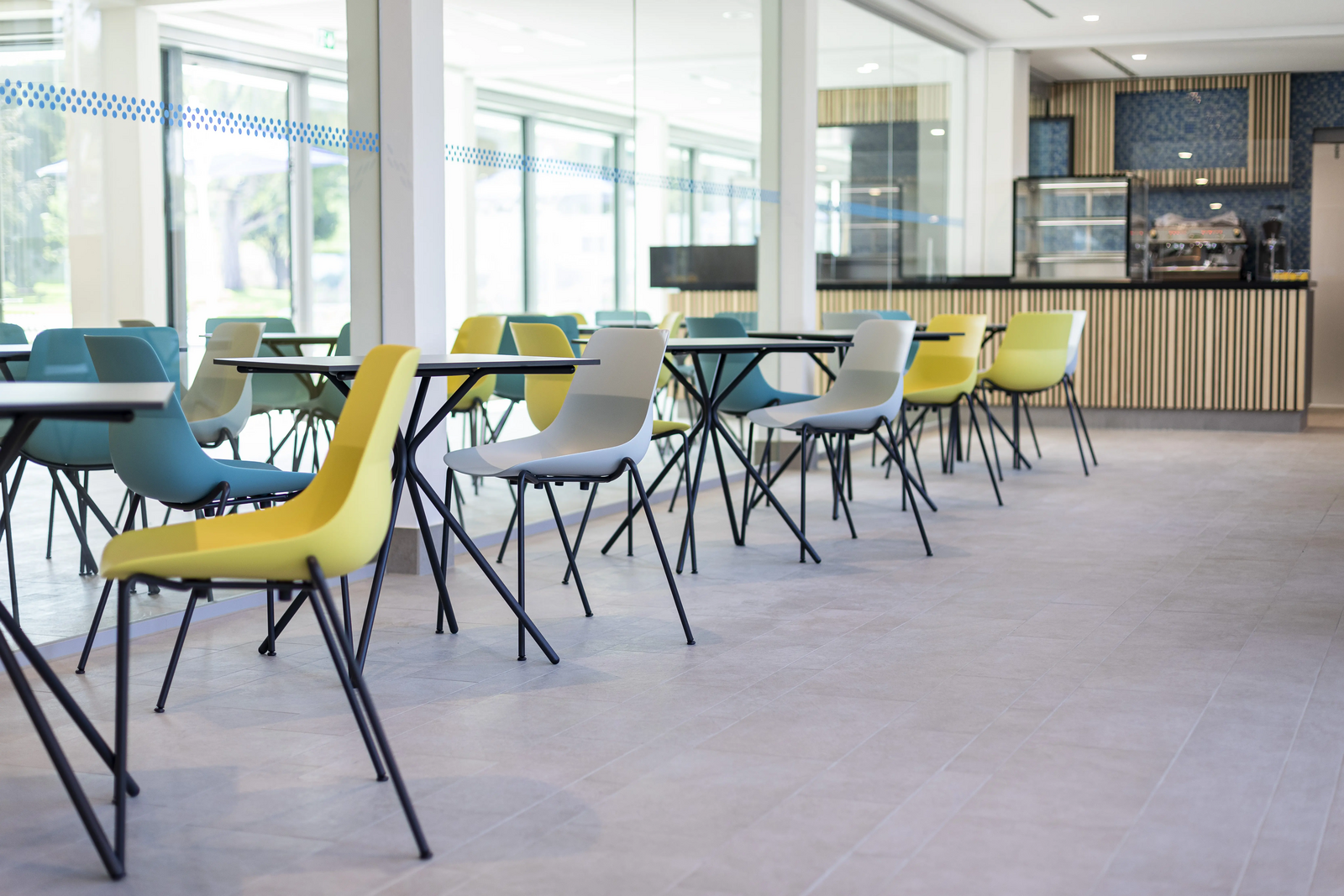 Mineralbad Berg Gastronomie innen Gastronomiebereich mit blauen, weißen und gelben Stühlen, Tischen und einer Theke im Hintergrund im Mineralbad Berg.