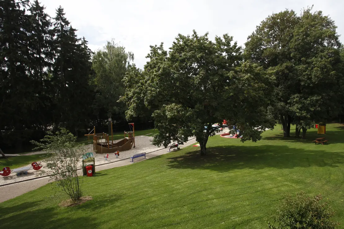 Außenansicht Spielplatz und Liegewiese mit Bäumen im Freibad Möhringen.